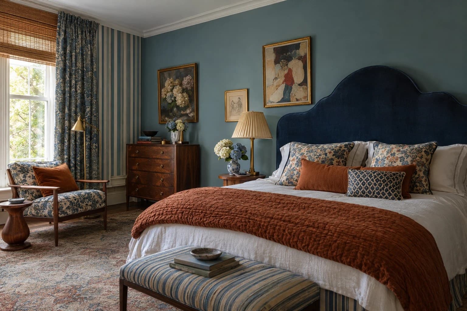 Newstalgia interiors: bedroom with blue-green walls, a navy velvet bedhead, a rust quilt, antique mahogany chest and mixed floral and striped textiles